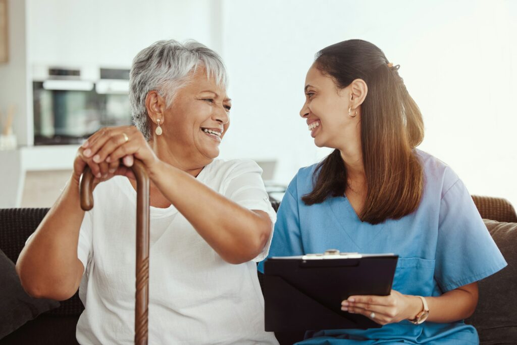 Senior care, healthcare insurance and caregiver woman sitting with elderly woman patient laughing a
